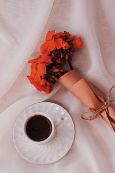 A delicate arrangement of coffee and vibrant flowers on white fabric surface, perfect for a warm and inviting atmosphere.
