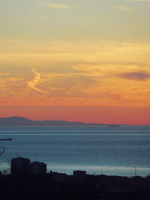 Free A breathtaking sunset over the ocean, with a silhouetted town and distant islands. Stock Photo