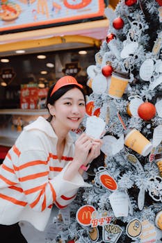 Smiling Asian woman decorating a Christmas tree with fast food theme at a food truck.