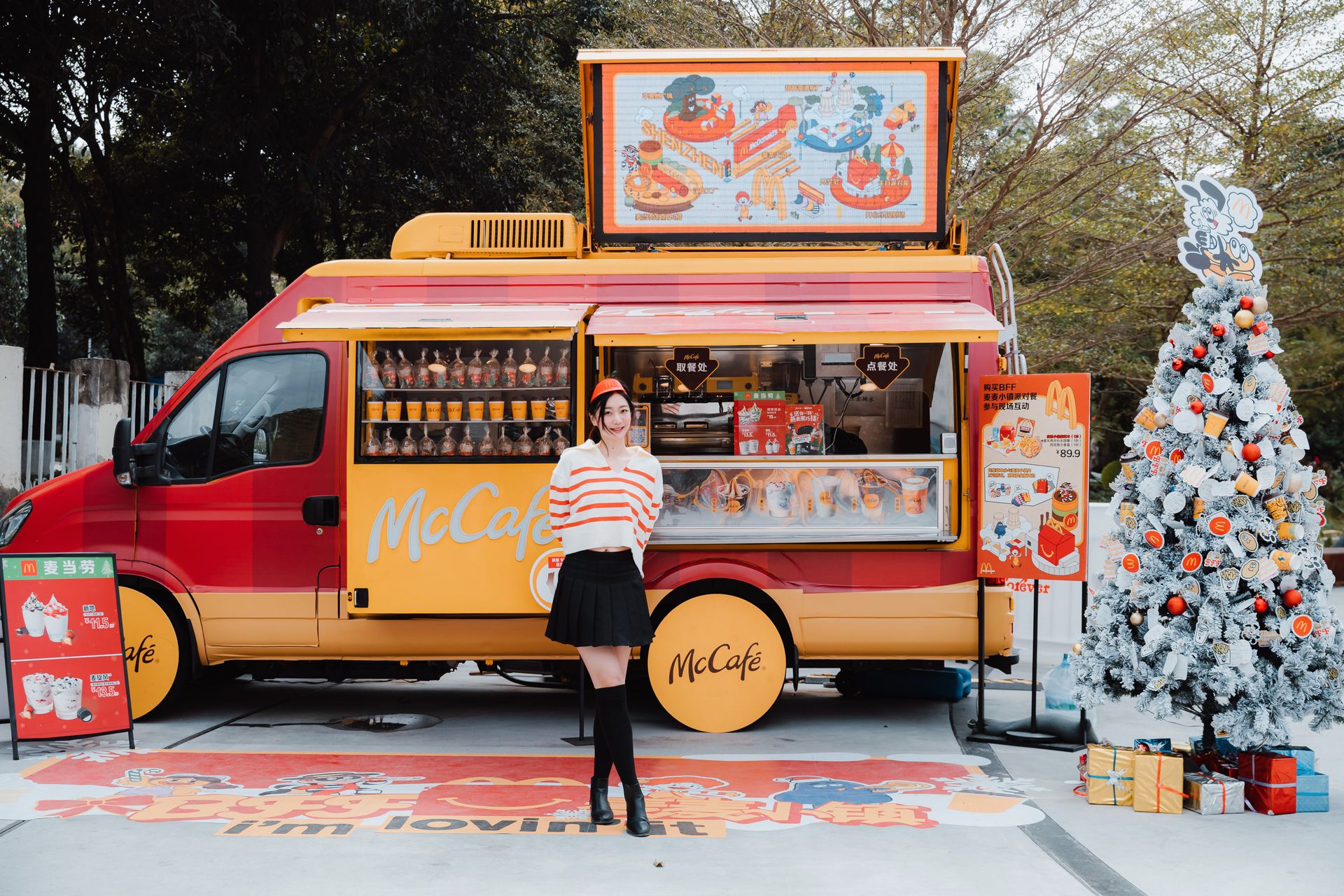 Woman standing by a McCafe food truck with Christmas decorations, creating a festive urban atmosphere.