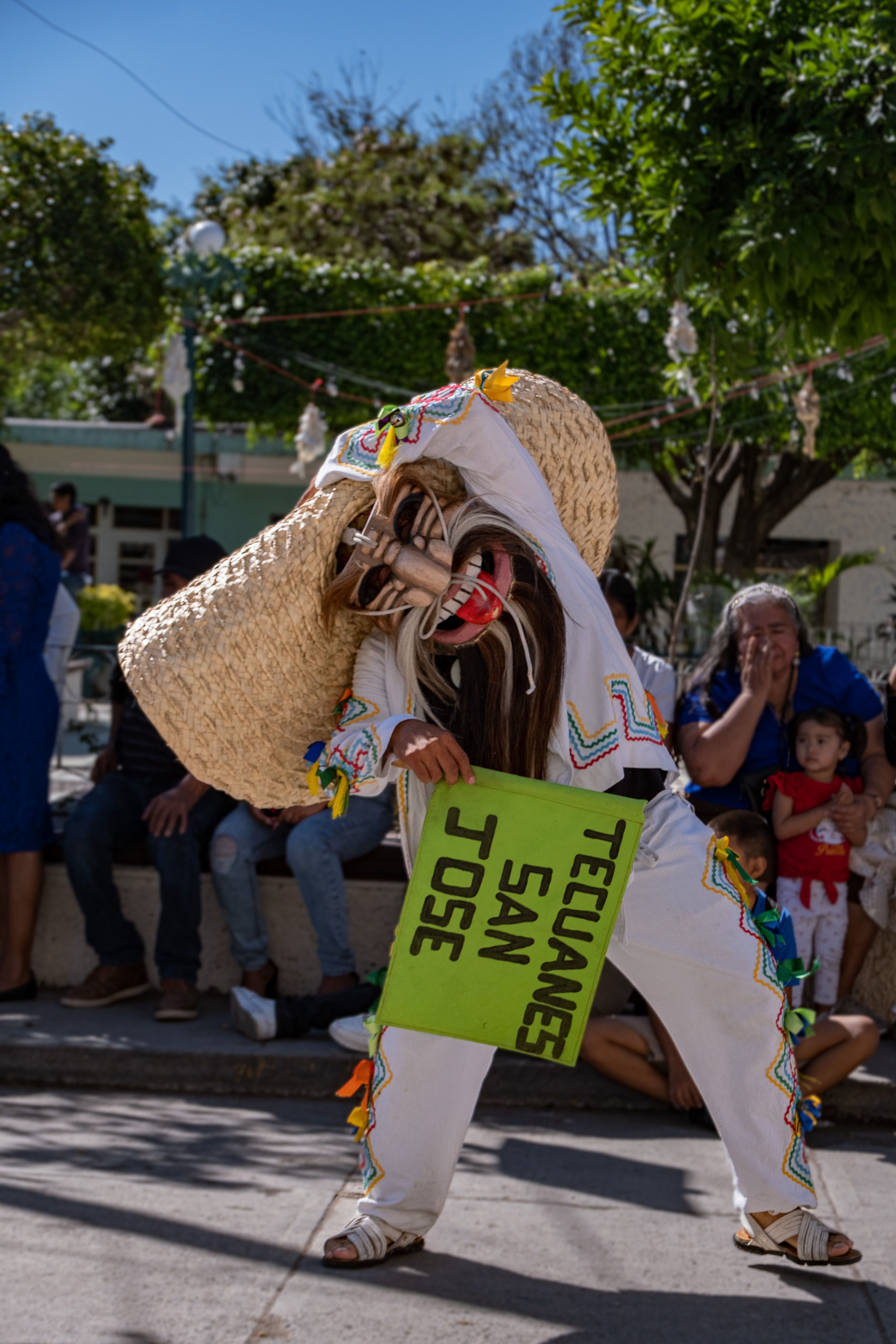 Colorful traditional dance performance with vibrant costumes and masks in a festive parade setting.