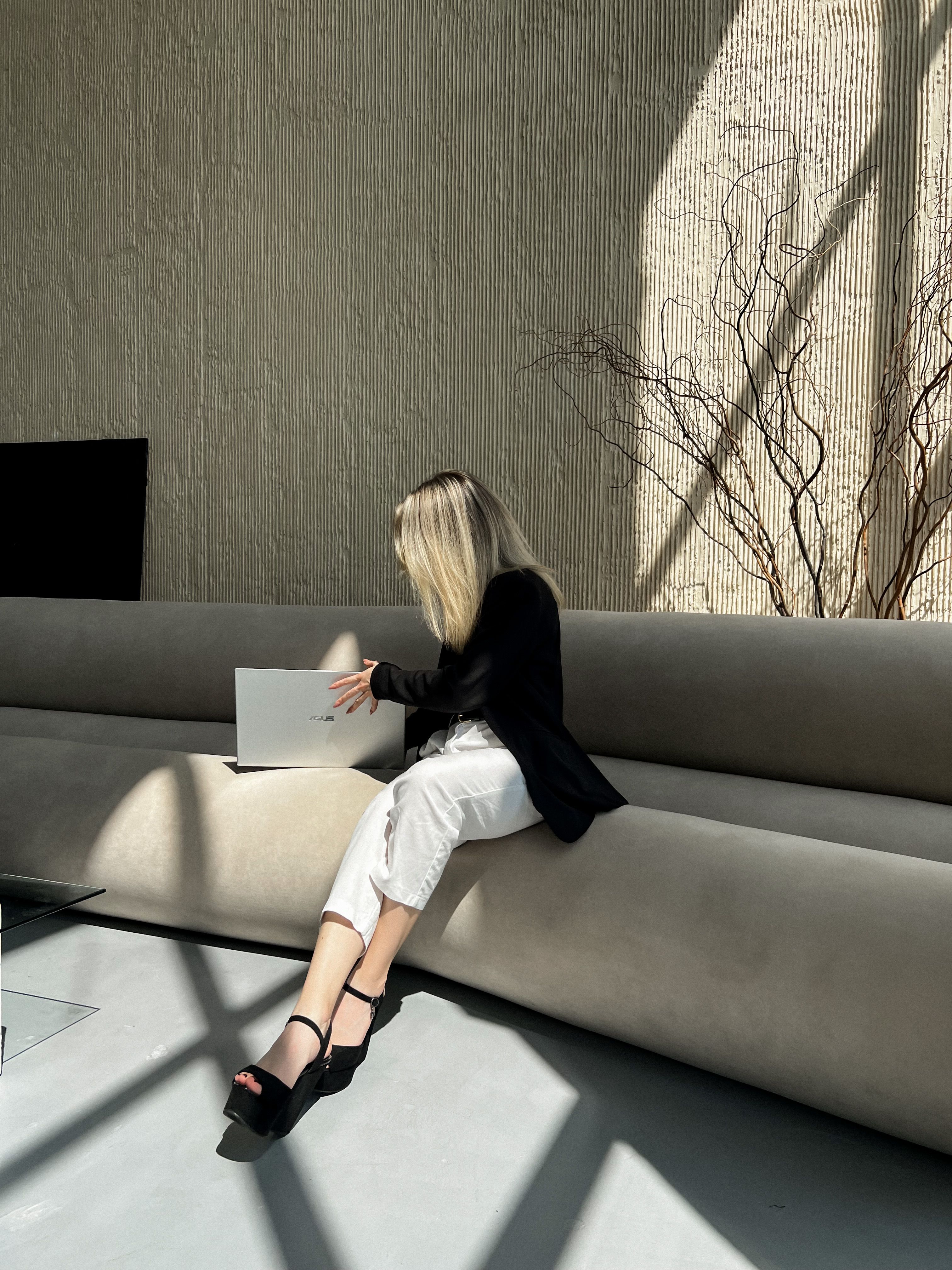 A stylish businesswoman using a laptop in a sunlit, modern office setting.