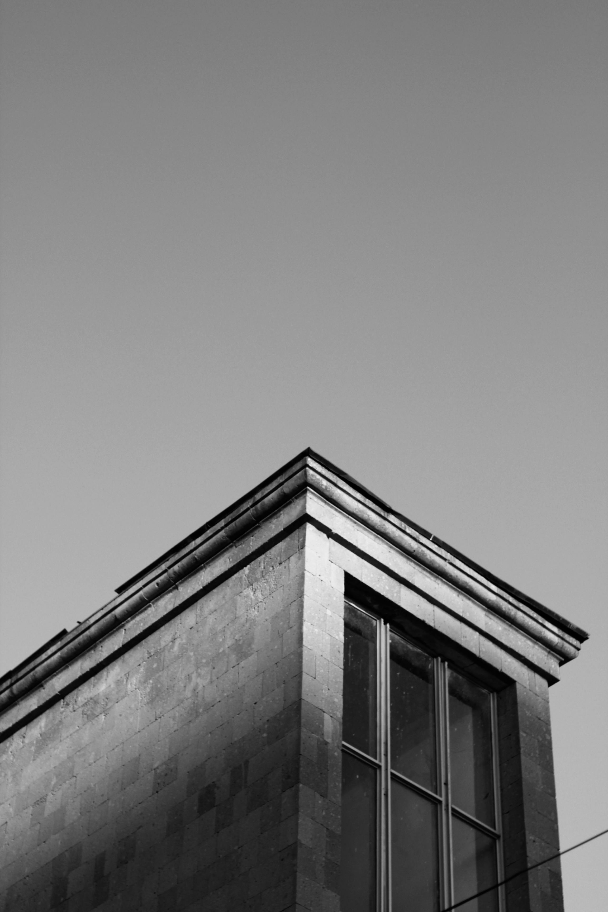 Free Black and white photo of a building corner with large windows against a clear sky. Stock Photo