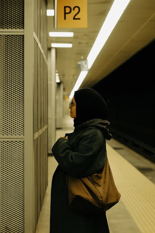 Free A woman in a black hijab and gray coat waits at a train station platform. Stock Photo