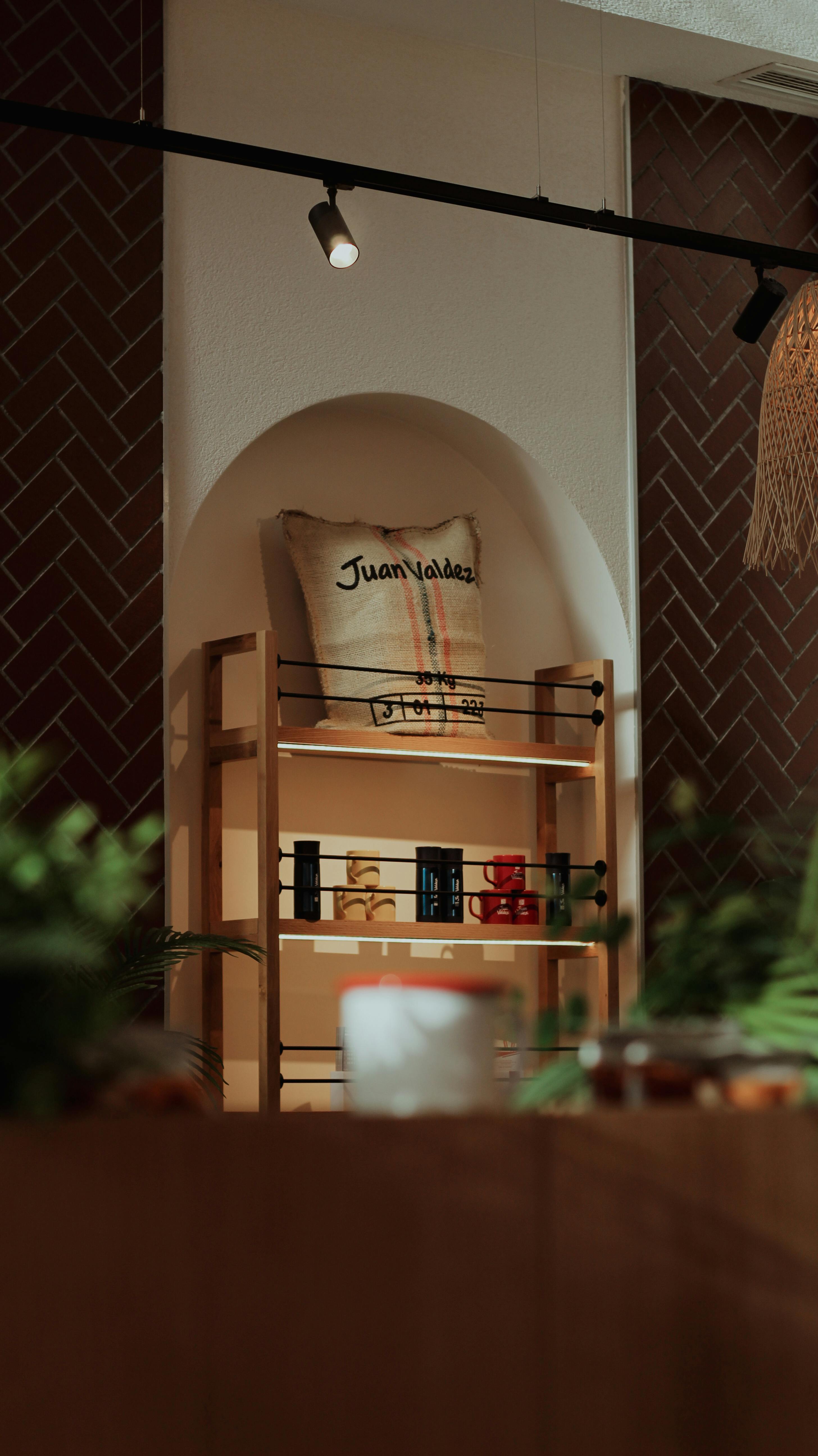 Warm cafe setting with wooden shelves and decorative pillow under soft lighting.