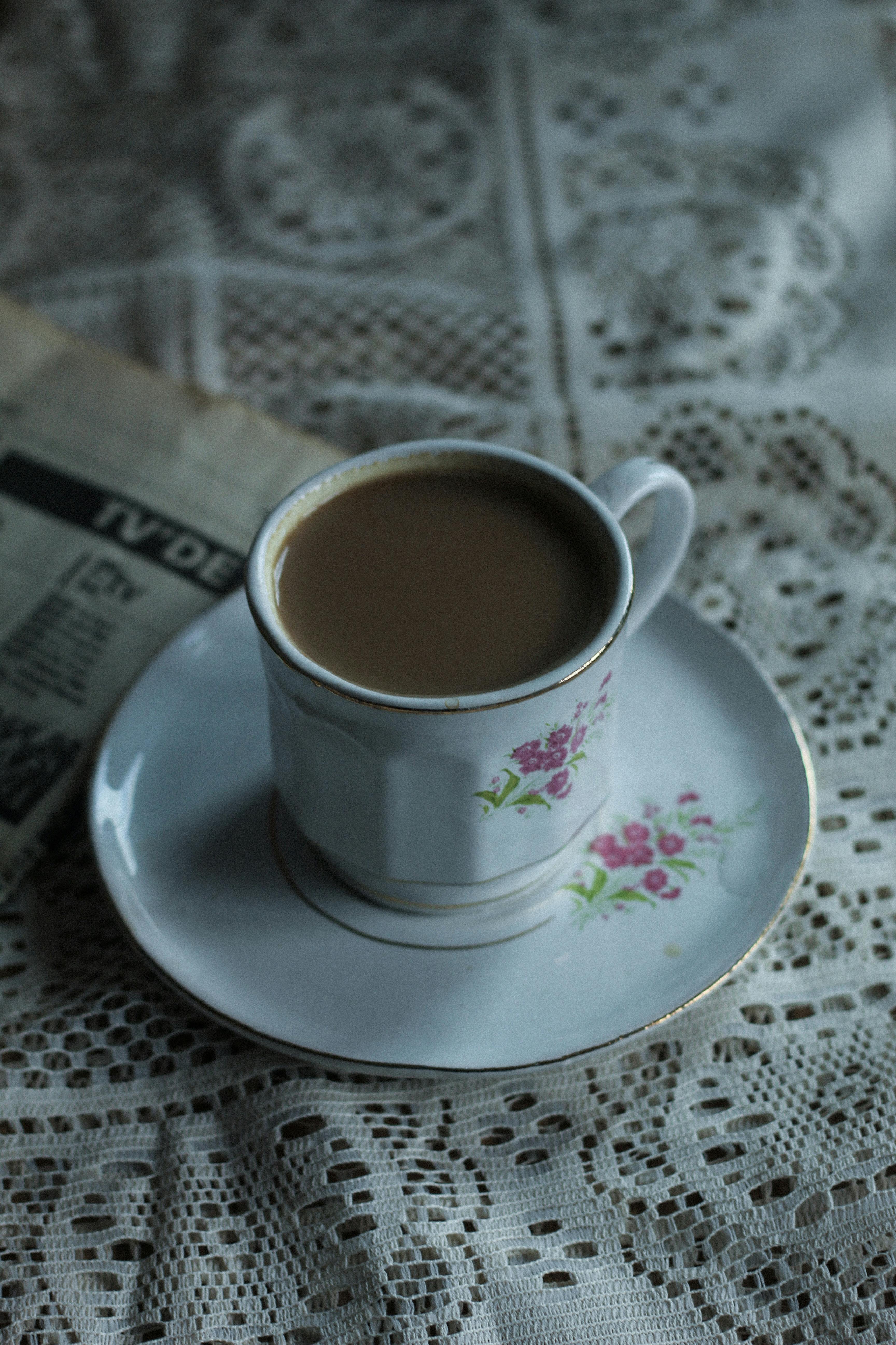 A floral cup of coffee rests on a lace tablecloth for a vintage and cozy vibe.
