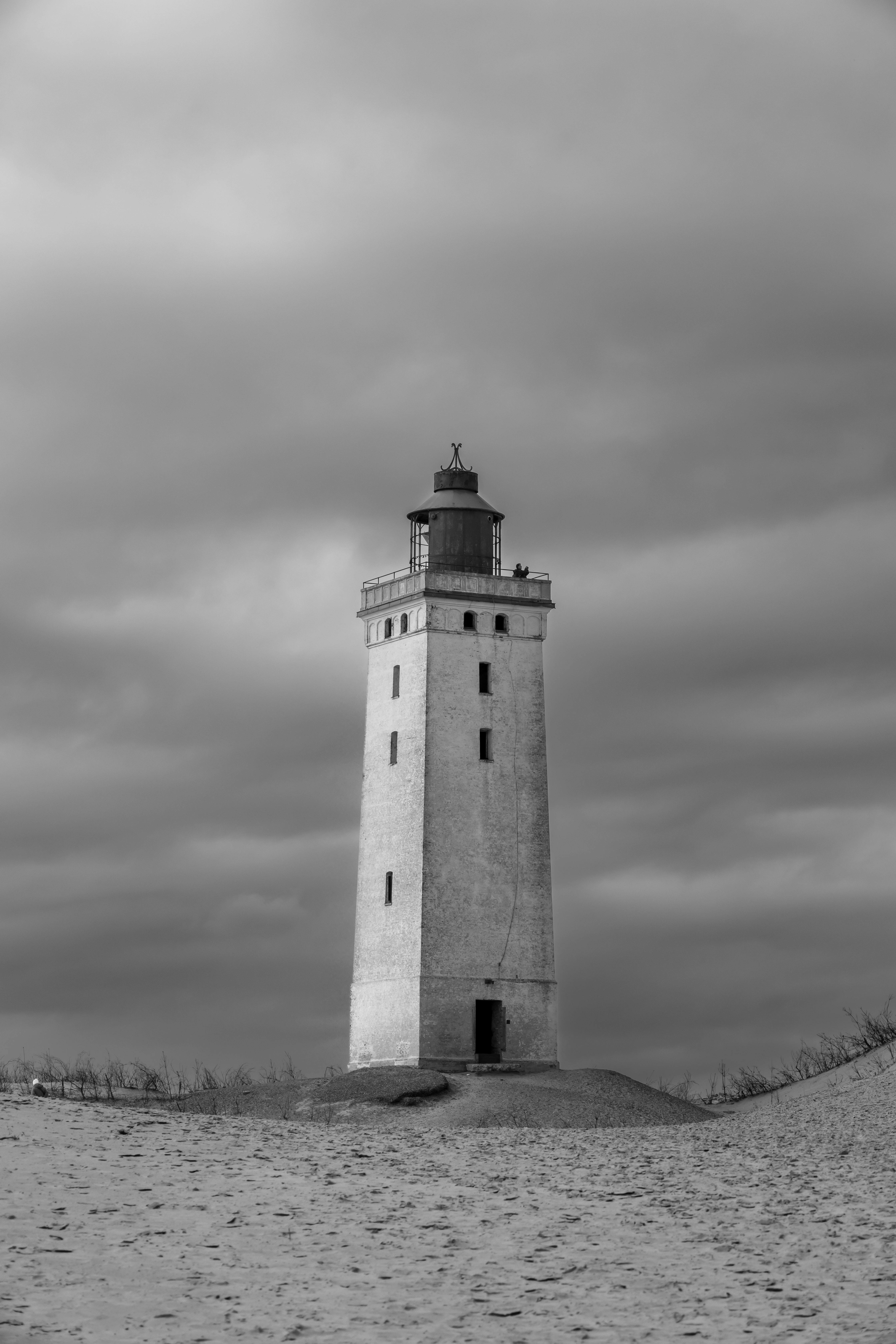 Black and white photo of a historic lighthouse in Løkken, Denmark, under a dramatic sky.