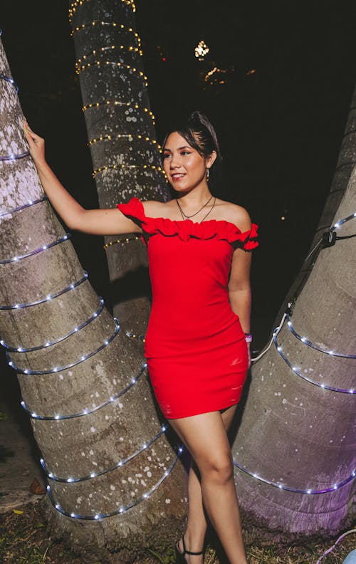 Young Woman in a Red Dress Standing Outside next to Trees with Lights at Night 