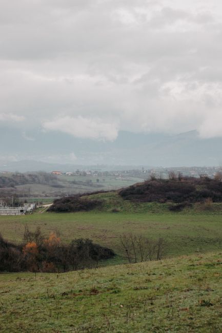 Peaceful rural scene with green fields and hills under cloudy skies, evoking tranquility.