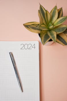 Minimalist 2024 planner with pen and indoor plant on a peach-colored background for productivity inspiration.