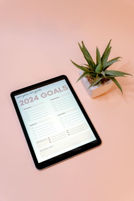 Flat lay of a tablet displaying 2024 goals beside a plant on a peach background.