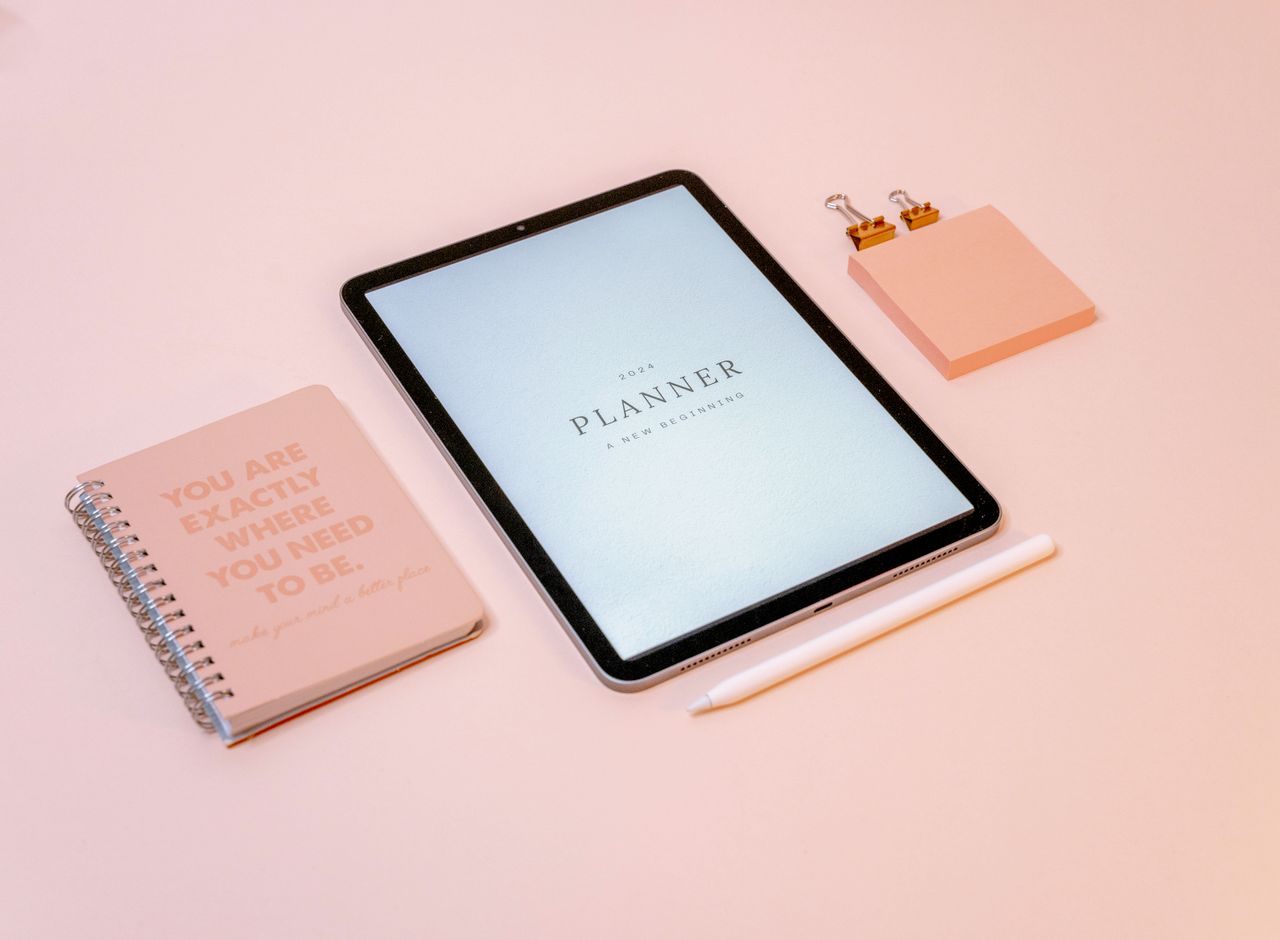 A stylish pink-themed desk arrangement with a 2024 planner, tablet, and journal