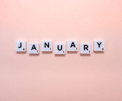Scrabble tiles spelling 'January' on a soft peach background, perfect for new year themes.