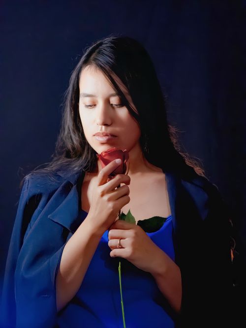 Free A young woman in a blue dress holds a rose, creating a serene and elegant portrait. Stock Photo