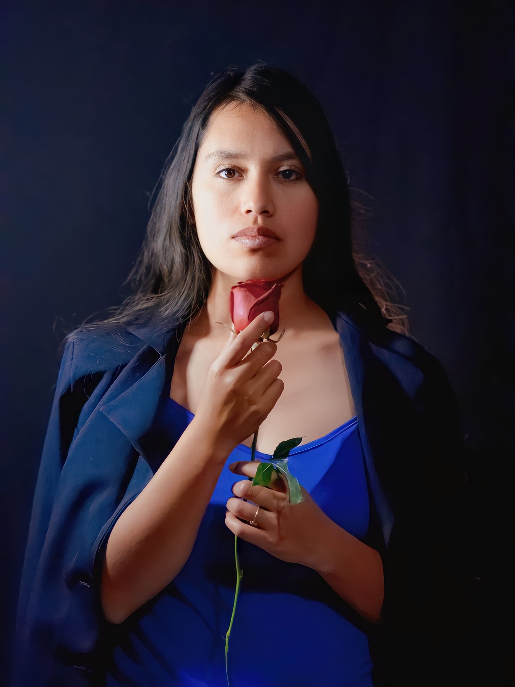Portrait of a woman in blue holding a rose, showcasing elegance and style.