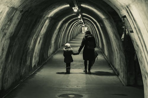 Woman and Girl Holding Hands Walking Through a Tunnel