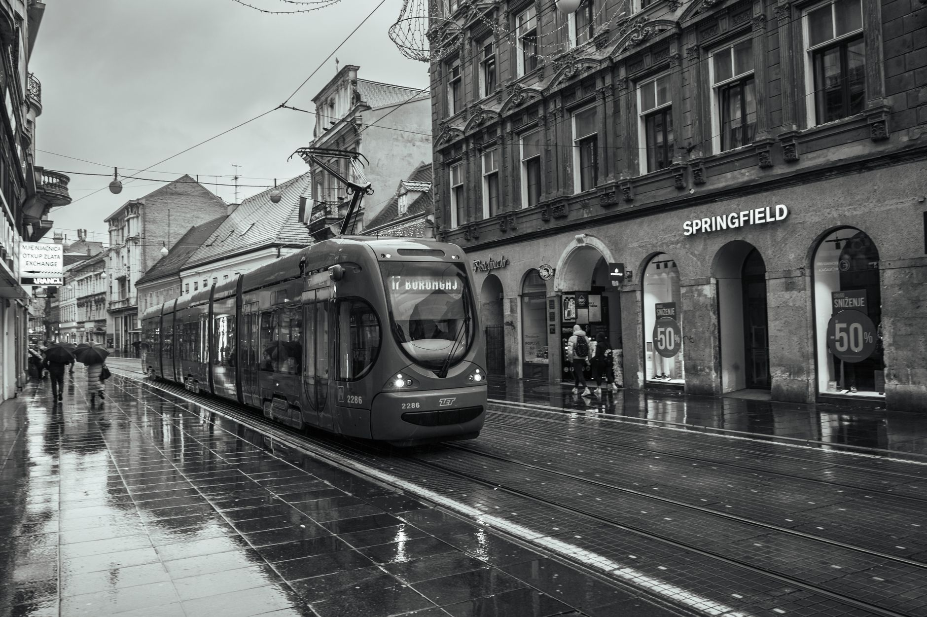 A sleek black and white tram travels down a rainy street in Zagreb, Croatia, capturing urban life.