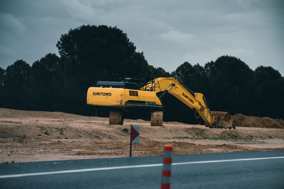 Yellow Sumitomo excavator working at a construction site near the road on a cloudy day.