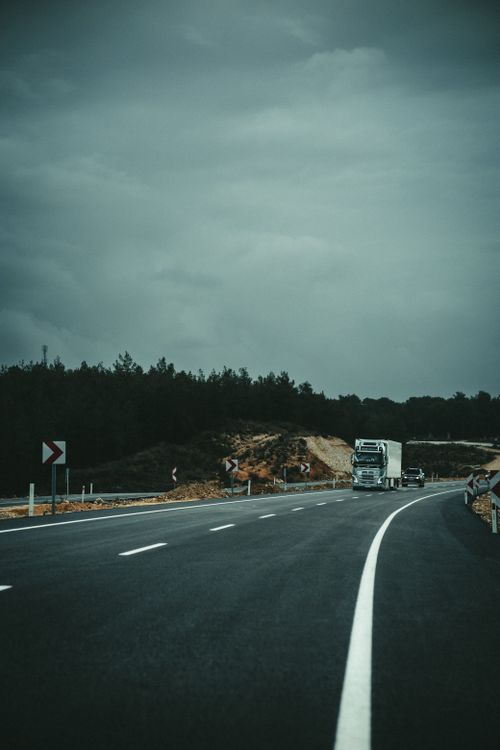 Free A solitary truck travels on a winding highway under a cloudy sky, embodying a sense of solitude and journey. Stock Photo