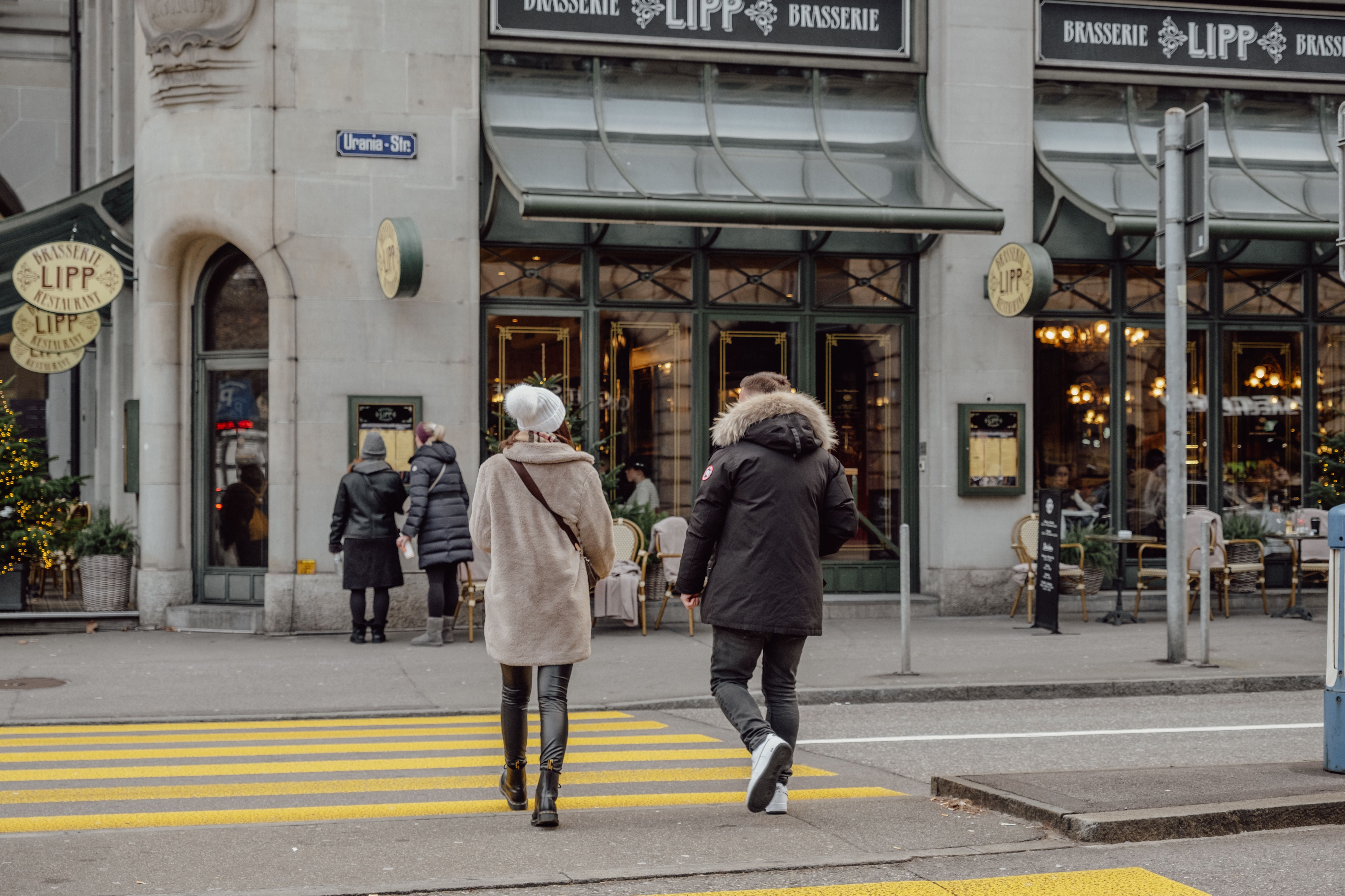 Adults crossing the street in front of Brasserie Lipp in Zurich, Switzerland.