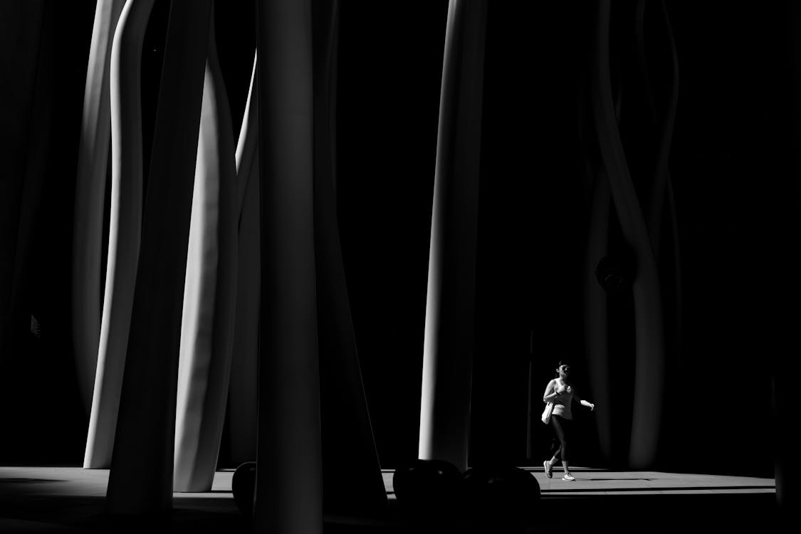 Grayscale Photo of Person Wearing Black Pants Walking Across Posts