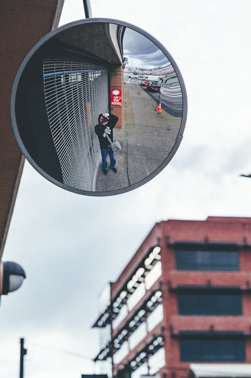 Reflection in Mirror of Man Standing on Sidewalk and Taking Pictures