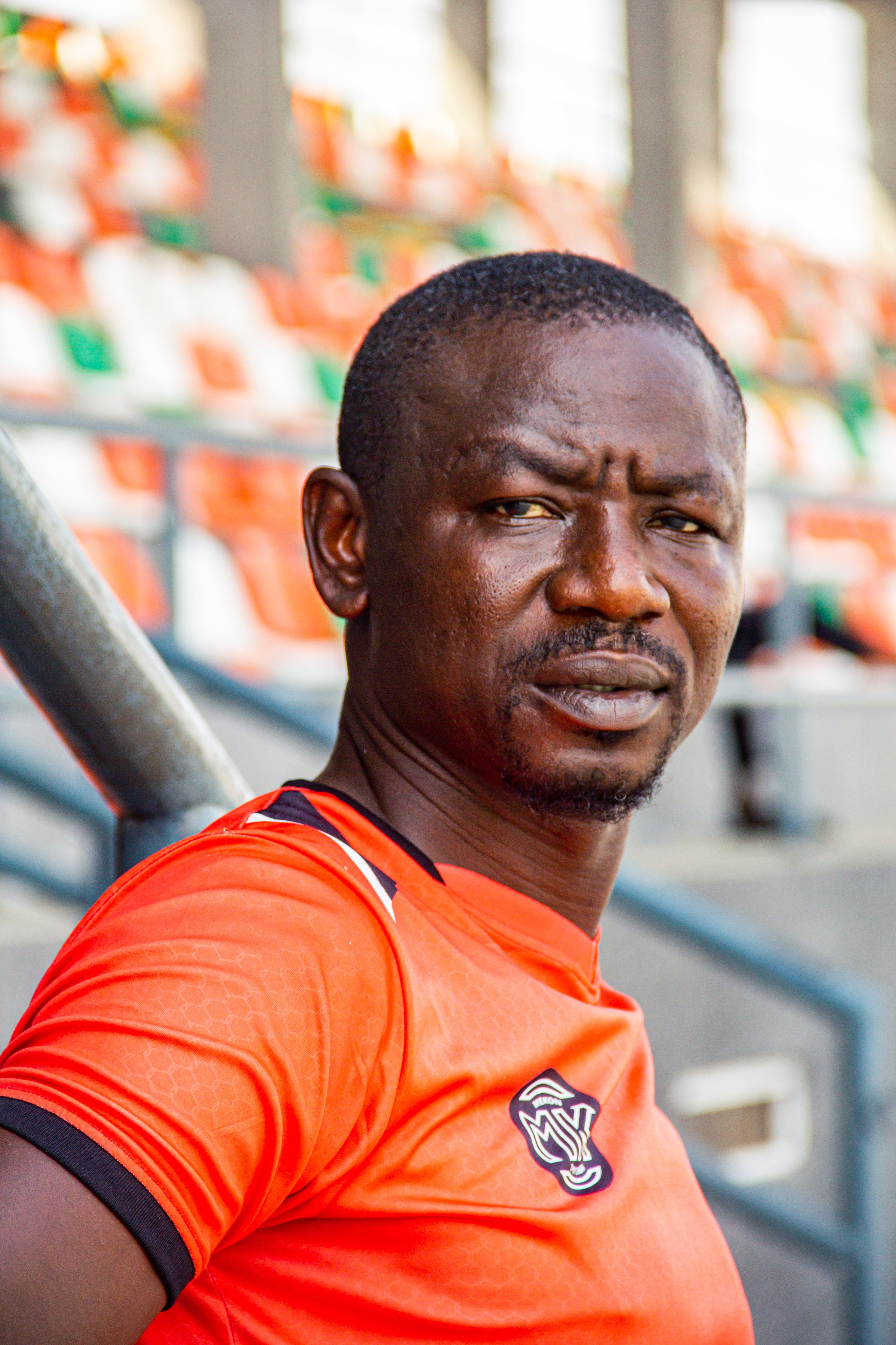 Close-up portrait of a male soccer player in a stadium wearing an orange jersey.