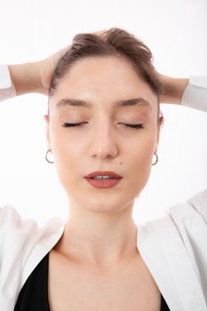 Serene portrait of a woman with closed eyes, hands on head, on a white background.