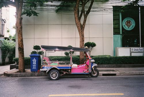 Free Colorful tuk tuk parked on a city street beside trees and buildings. Stock Photo