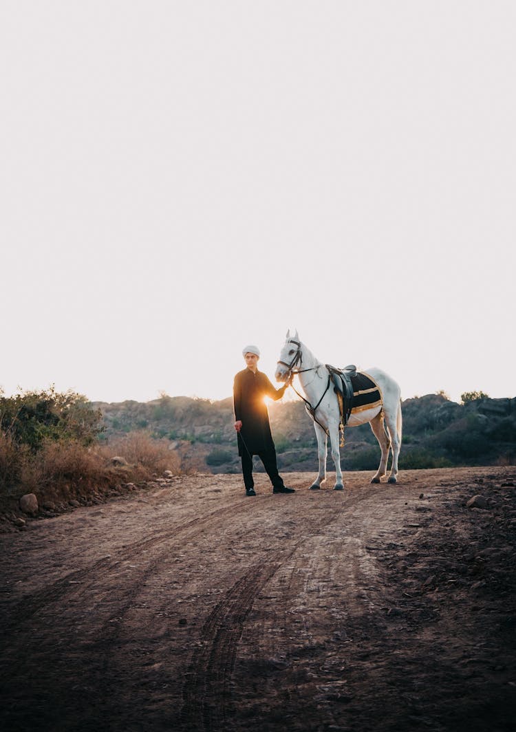 Man With A Saddled Horse On A Dirt Road At Sunset