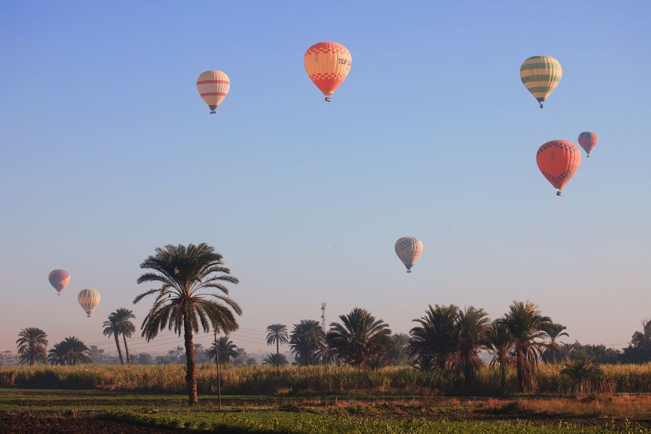 Hot Air Balloon Ride Over Nile Fields At Dawn. hot air balloon ride over Nile River fields, wide open landscape setting, people present as small silhouettes, dawn light.