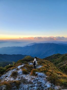 Back view of a hiker standing on a mountain, enjoying a scenic sunset view.