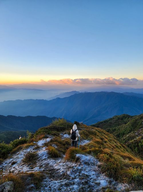 Free Back view of a hiker standing on a mountain, enjoying a scenic sunset view. Stock Photo