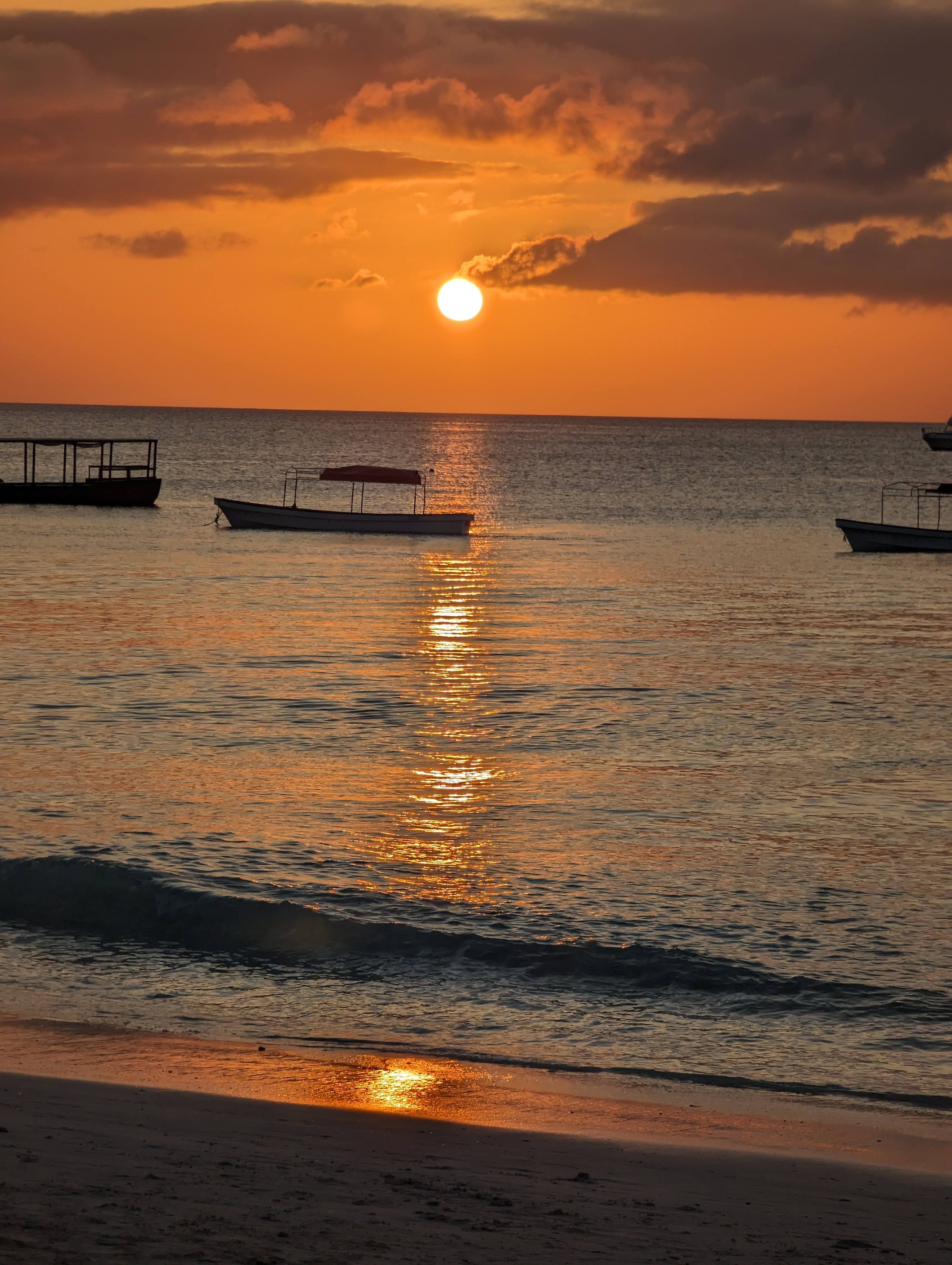 Beautiful sunset over a calm beach in Zanzibar, Tanzania with boats silhouetted against the orange sky.