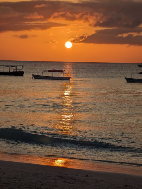 Free Beautiful sunset over a calm beach in Zanzibar, Tanzania with boats silhouetted against the orange sky. Stock Photo