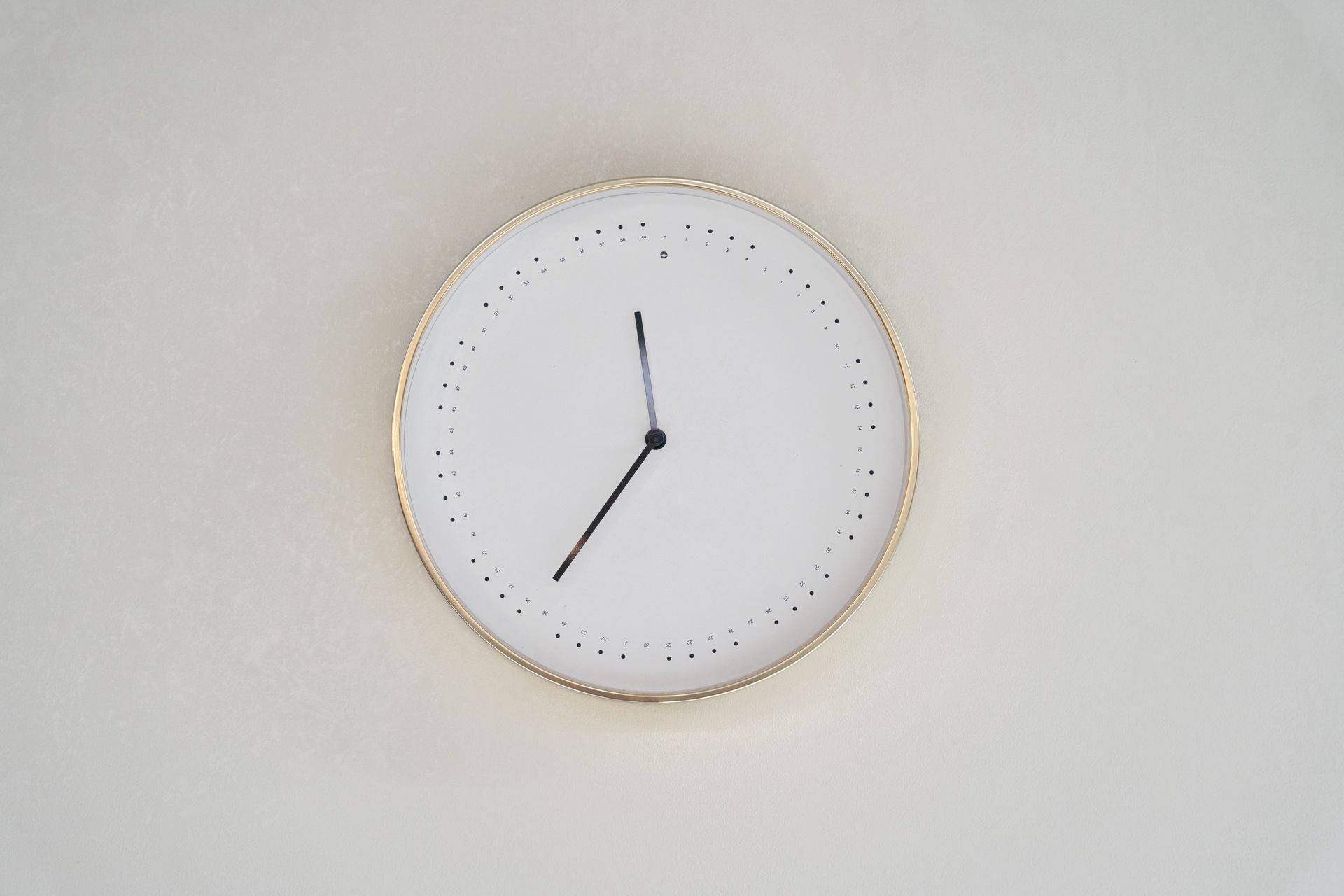 A minimalist design wall clock with a gold rim and no numbers on a neutral background.