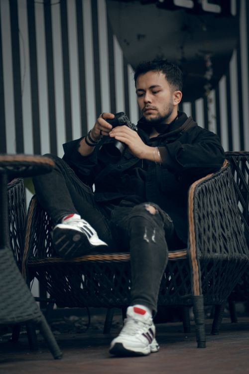 Free A stylish young man sits in an armchair checking his camera, creating a relaxed and cozy vibe. Stock Photo