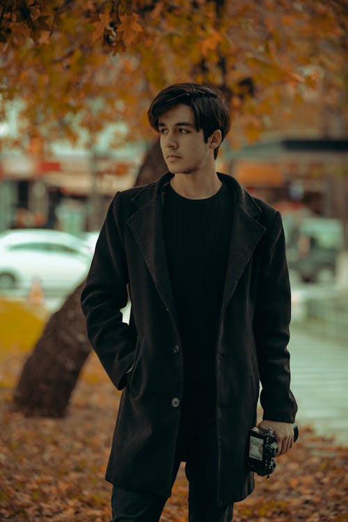 Young Man in a Coat Standing in a Park in Autumn 