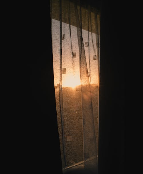 View of Bright Setting Sun behind a Window with a Curtain 