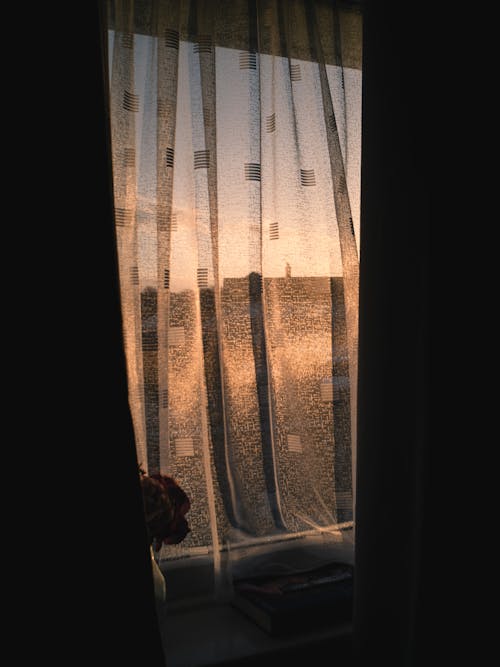 View of Bright Setting Sun behind a Window with a Curtain 