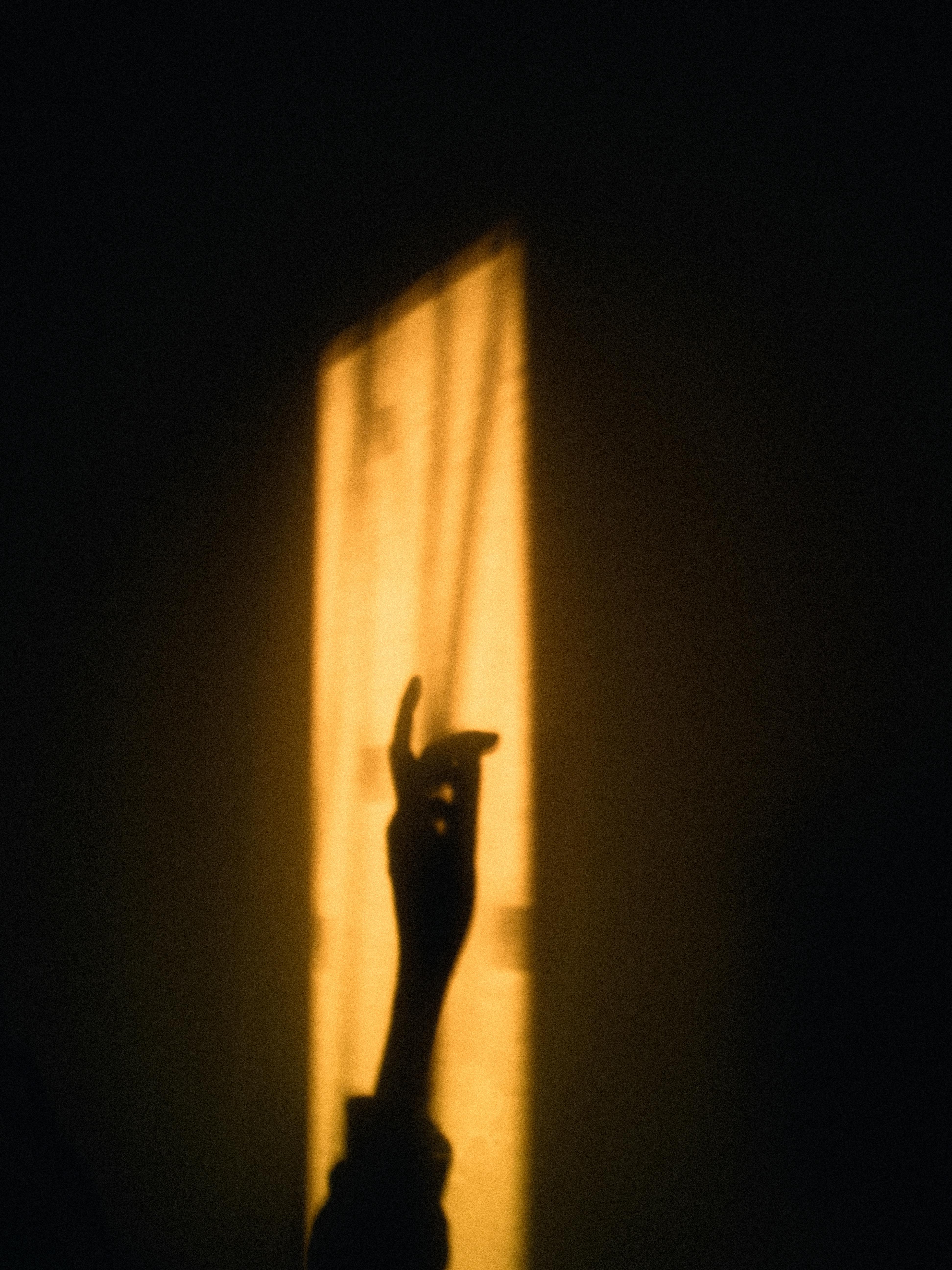 Silhouette of a hand casting shadows on a wall, illuminated by warm sunset light.