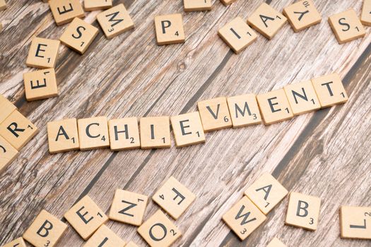 Scrabble tiles spelling 'Achievement' on a wooden surface.