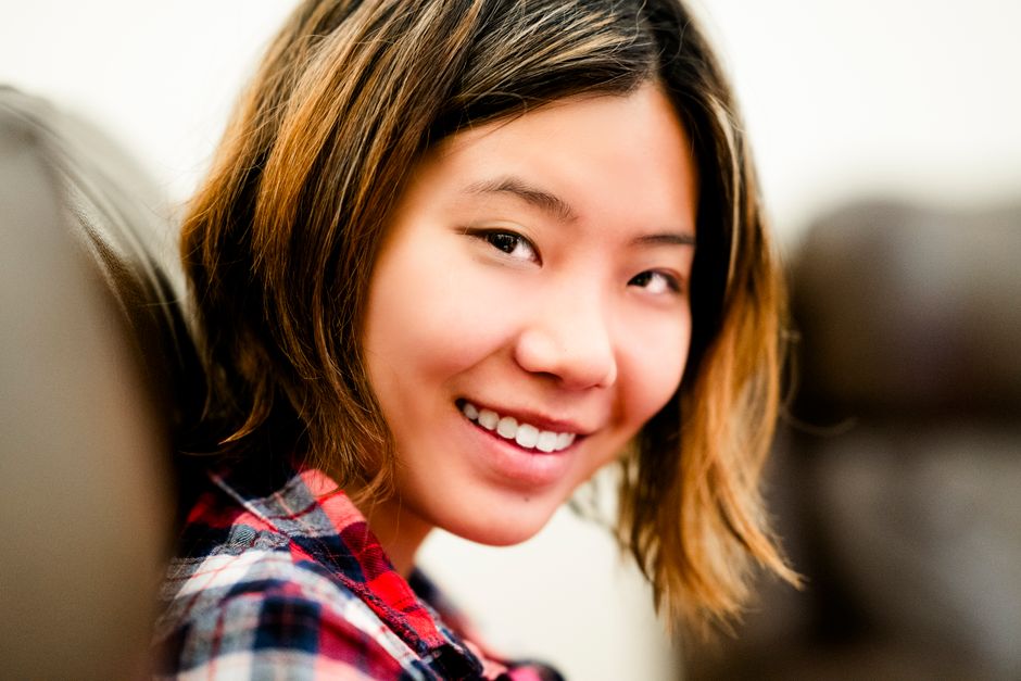Close-up portrait of a smiling young woman wearing a plaid shirt indoors.