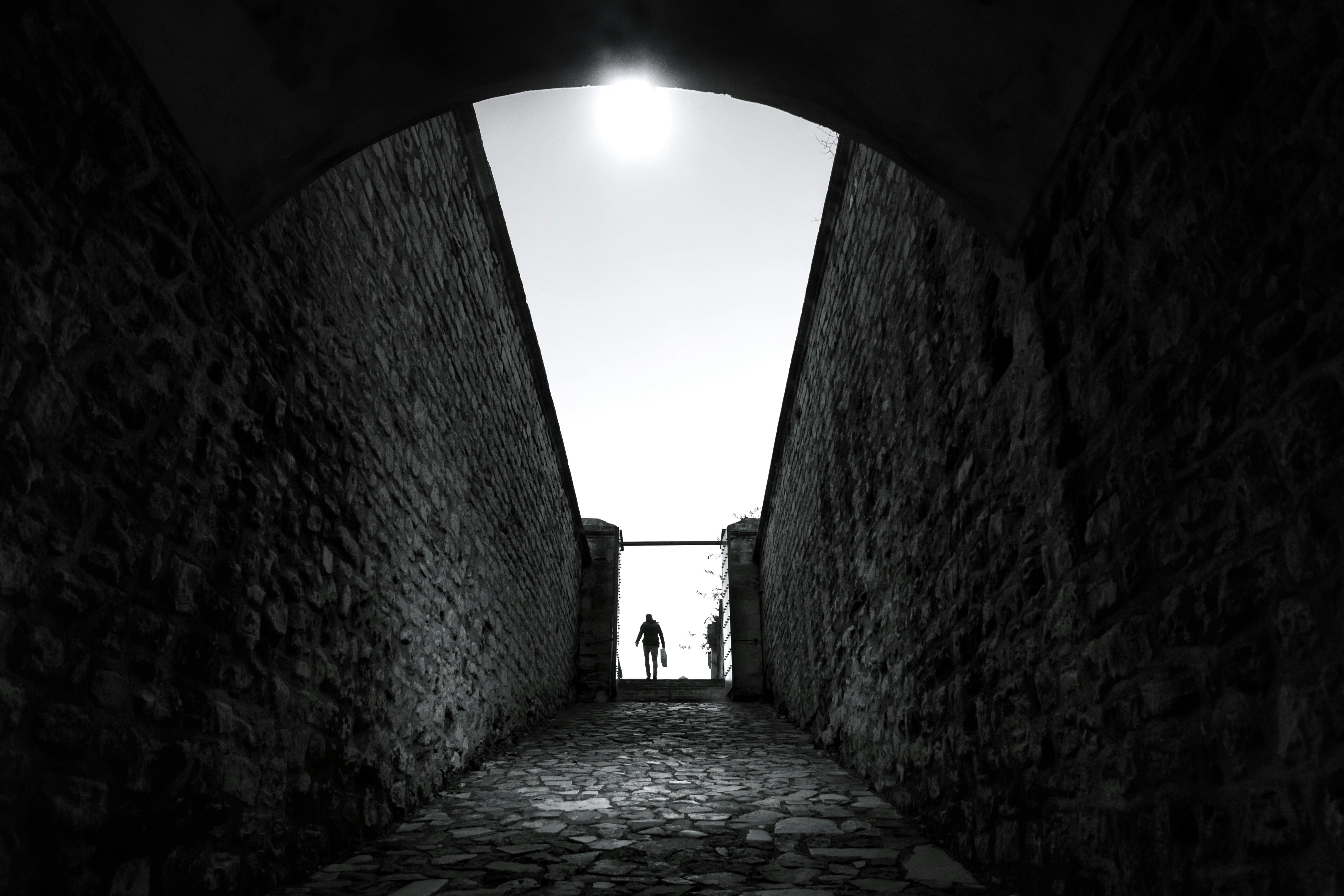Dramatic black and white silhouette of a person in a stone archway with sunlight above.