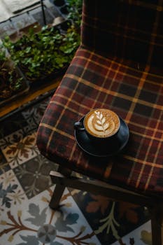 A beautifully crafted latte with delicate latte art on a plaid chair, perfect for a cozy setting.