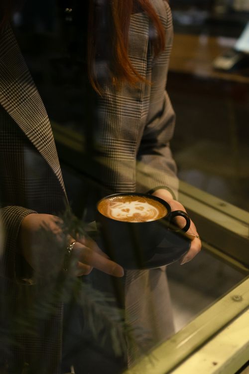 Free Woman holding a cappuccino cup near a window, creating a cozy atmosphere. Stock Photo