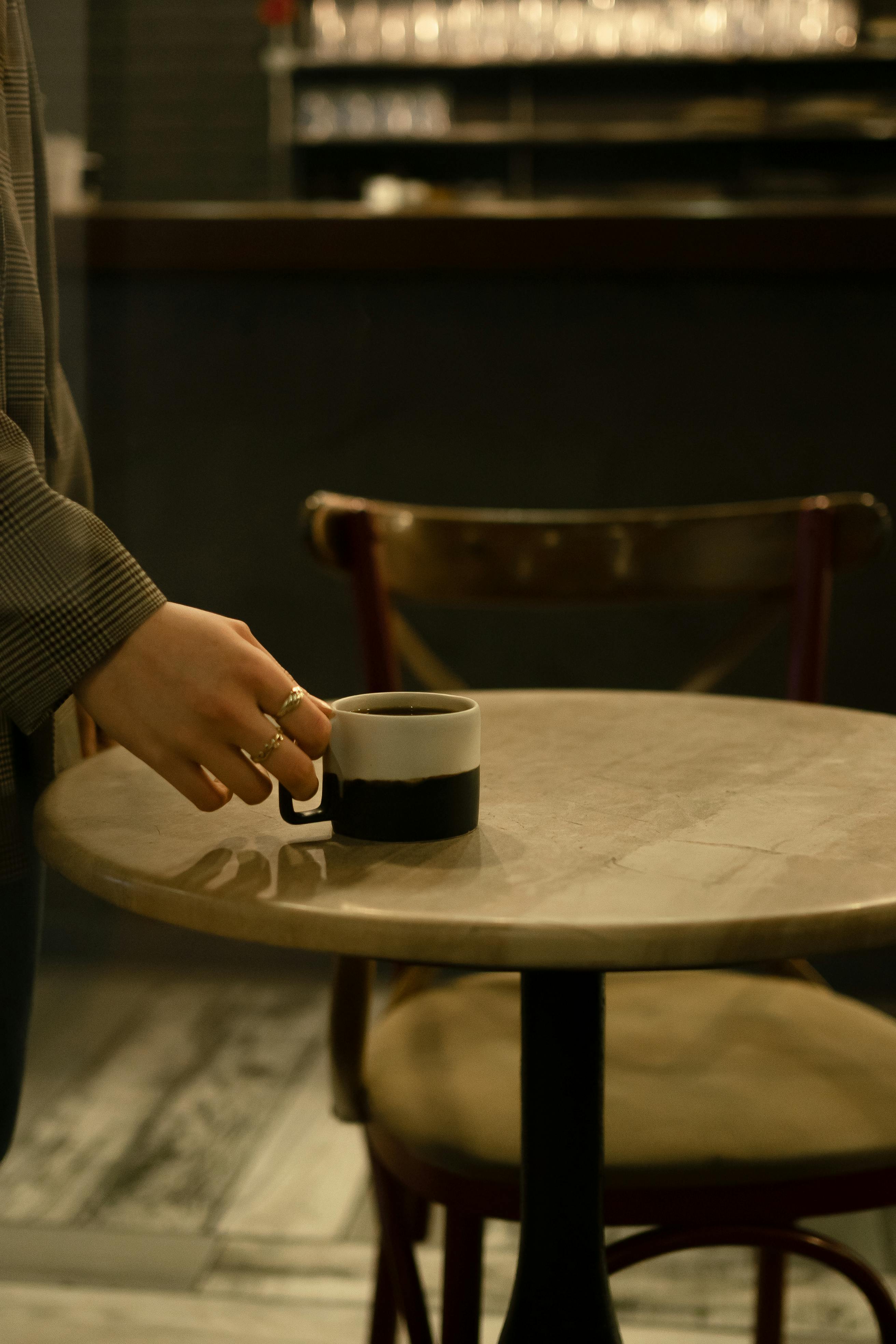 A warm scene in a café with a hand placing a coffee cup on a wooden table.