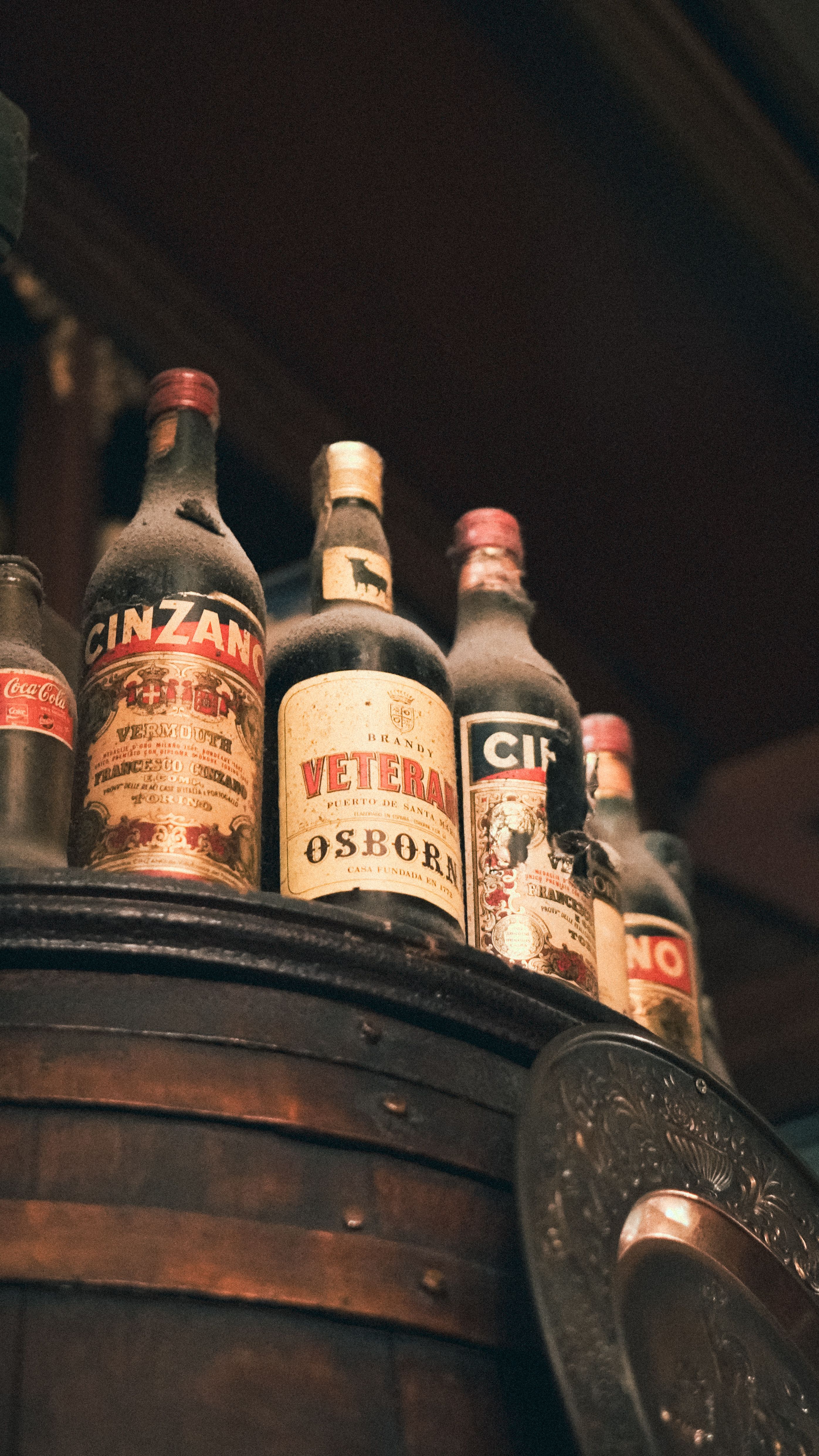 A collection of vintage liquor bottles arranged on a rustic wooden barrel in a bar setting.