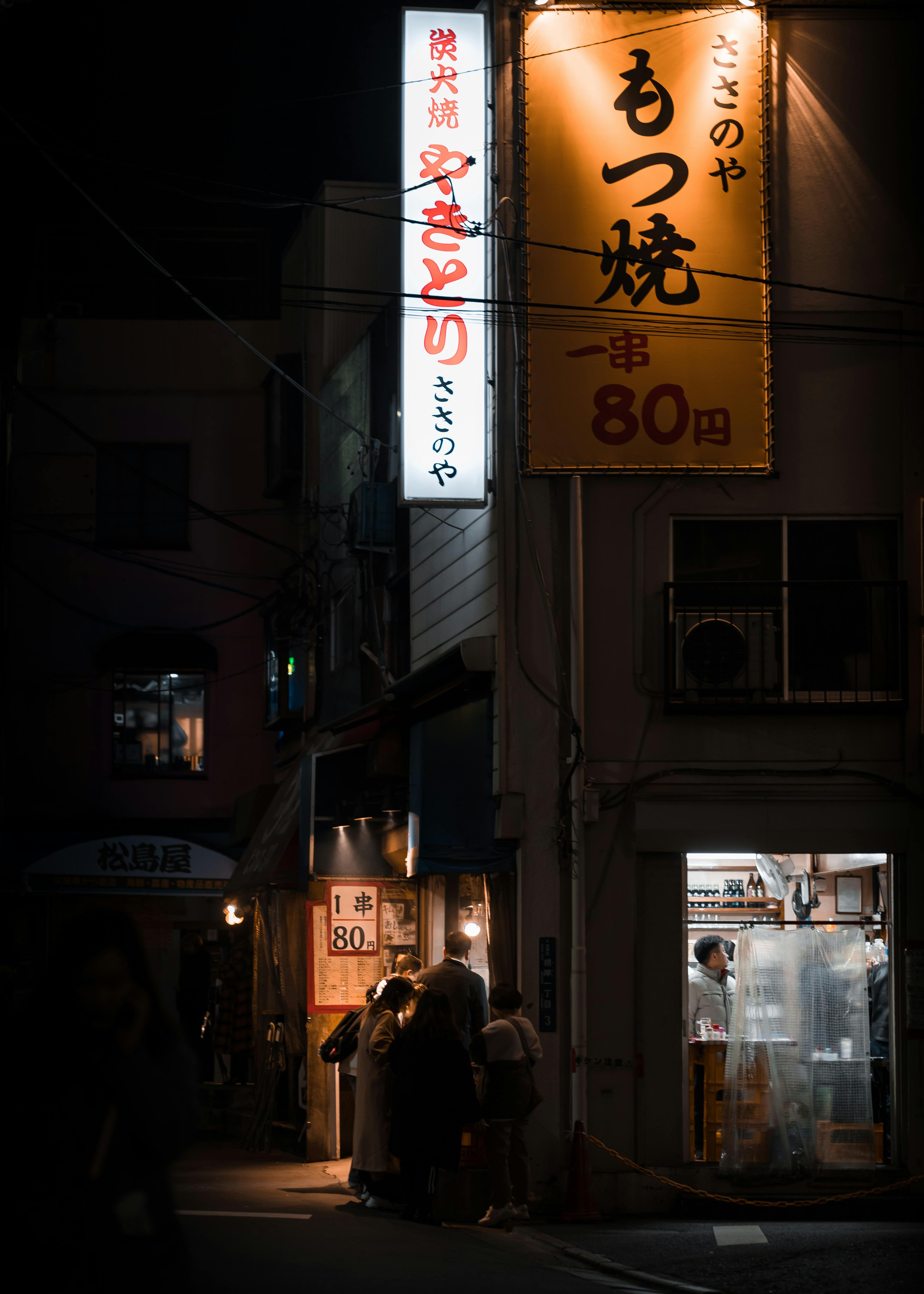 Bustling nighttime street in Tokyo with glowing neon signs and people gathering outside shops.