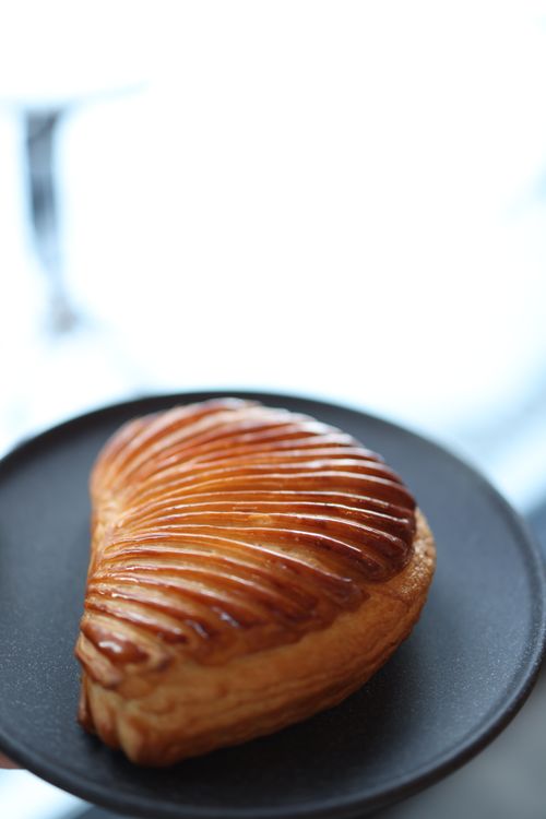 Free Close-up of a flaky, glazed puff pastry on a black plate, showcasing its golden-brown texture. Stock Photo